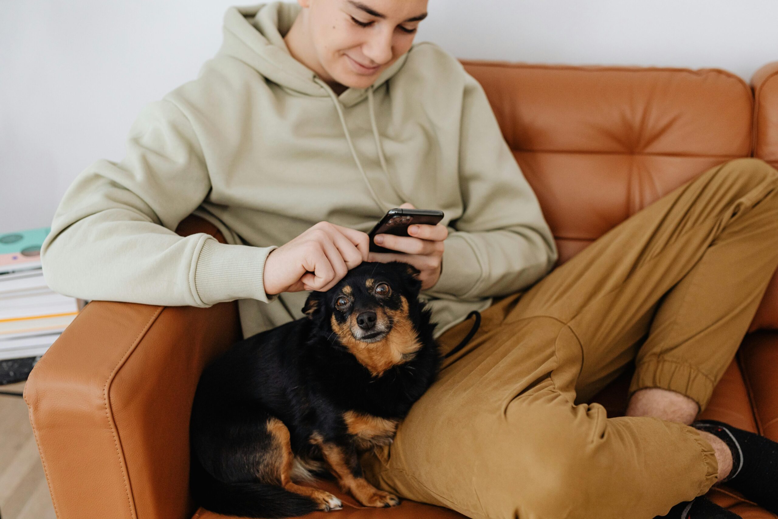 Home Teenager relaxes on couch with smartphone and pet dog.